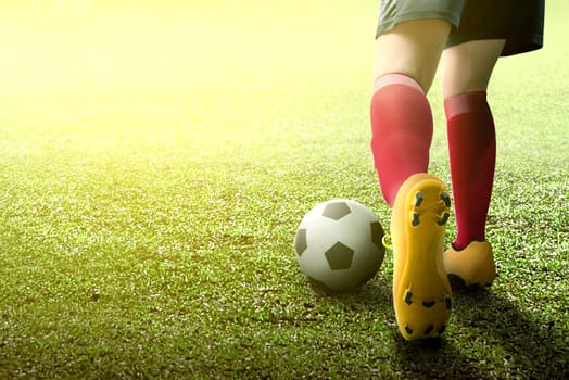 Rear view of football player woman in orange jersey kicking the ball on the green field