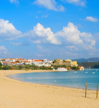 View of traditional village and people relaxing on beach in bright sunlight, Vila de Milfontes, Alentejo, Portugal