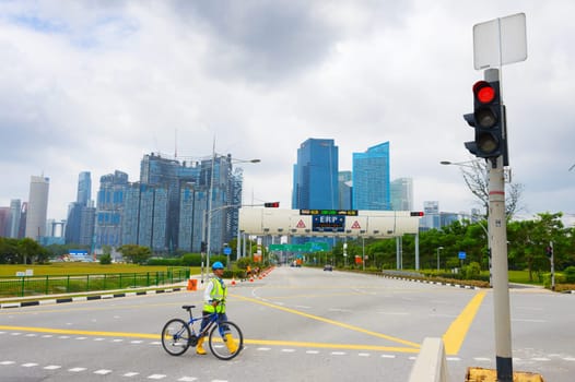 SINGAPORE - FEBTUARY 16, 2017: Construction site worker in helmet and vest crossing road with bicycle, Singapore downtown skyline in background