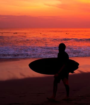 Surfer with surfboard walking by the ocean beach. Bali island, Indonesia