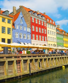 Old town with Nyhavn harbor view in bright sunny day, tourists walking and sitting in bars, cafes, restaurants by canal, Copenhagen, Denmark