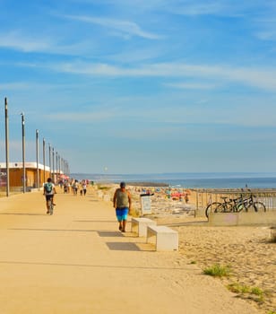 COSTA DA CAPARICA, LISBON, PORTUGAL - SEPTEMBER 17, 2018: People walking by seaside promenade in the sunny summer day. Costa de Caparica is the famous tourist destination