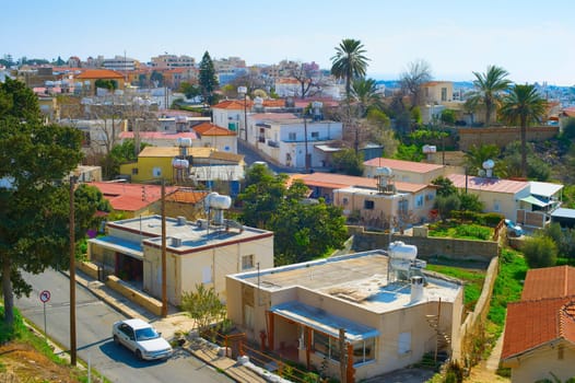 Aerial skyline of Paphos town in sunlight, car on road among houses of typical architecture, palms and green trees, Cyprus