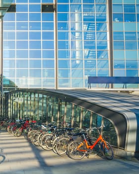 Parking of bicycles by Kastrup airport entrance under canopy, glass building facade in evening sunshine, Copenhagen, Denmark