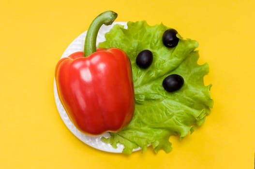 Bell pepper, olives, salad lettuce on white plate on yellow background