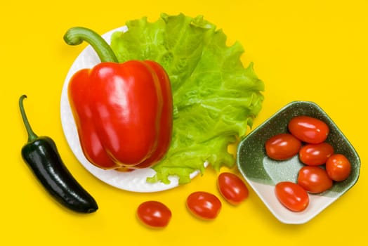 still life of jalapeno pepper,  bell pepper, tomato cherry, lettuce on yellow background