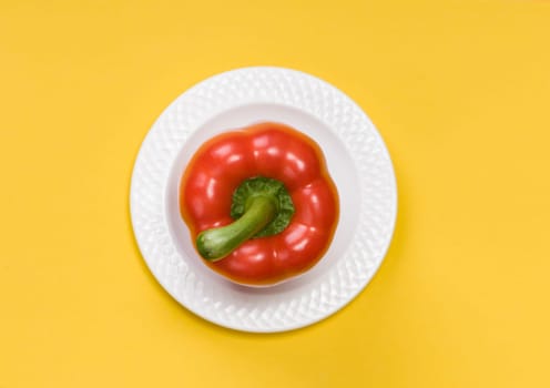 single red bell pepper on white plate  on yellow background