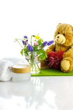 Towels next to a cream jar in front of white background and flowers in a vase.
