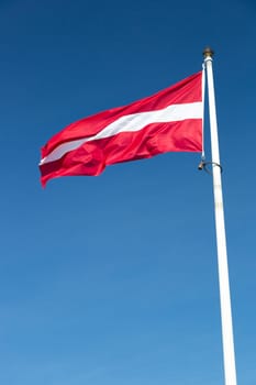 The Flag of Latvia waving in the wind with a clear blue sky.