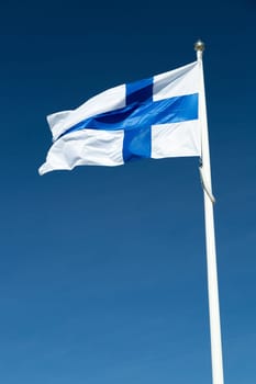 The Finnish Flag on a Flagpole waving in the wind with a blue sky.
