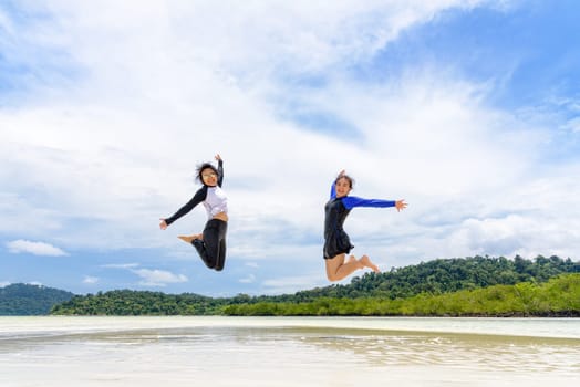 Happy two asian teen girls friends jumping enjoy on the beach of Ko Ra Wi on blue sky background during the sea tour vacation in summer holiday at Ko Lipe island, Tarutao National Park, Satun, Thailand