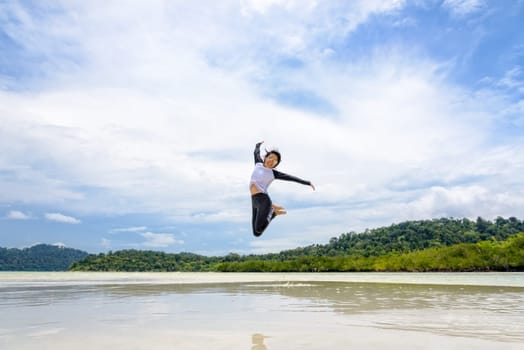 Happy asian young woman wearing sunglasses jumping fun on the beach of Ko Ra Wi on the blue sky by the sea in vacation summer holiday at Lipe island in Tarutao National Park, Satun, Thailand