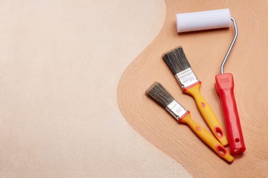 Yellow paint brushes and red roller lying on textural double background consisting of two beige shades. Top view with copy space, Concept of construction or design office