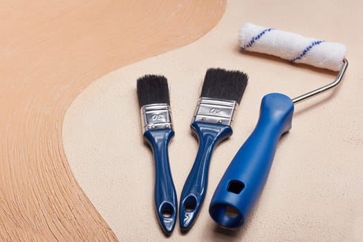 Blue paint brushes and roller lying on textural double background consisting of two beige shades. Top view with copy space, Concept of construction or design office