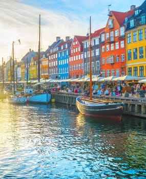 Nyhavn view with boats by embankmentat sunset, people walking and sitting at restaurants, Copenhagen, Denmark