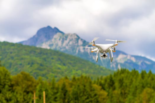 White drone quad copter with high resolution digital camera flying in the blue sky over the mountain