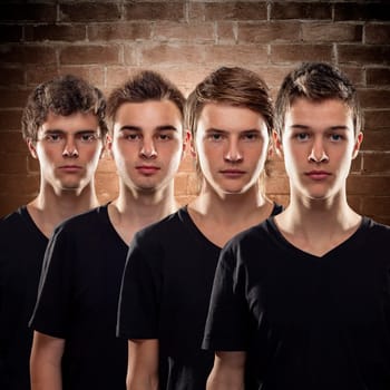 Group of young friends and serious teenagers stand behind each other in front of a brick wall
