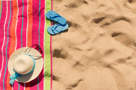 Beach towel with hat, sun glasses and flip flops on sand