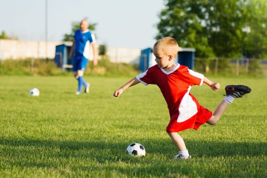 The 4 years old boy is shooting the soccer ball on soccer sport training outdoors on playing field.