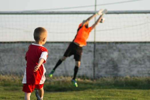 The little 4 years old boy as soccer player is kicking a goal to goalkeeper outdoors on playing field. Soccer sport training for children concept.