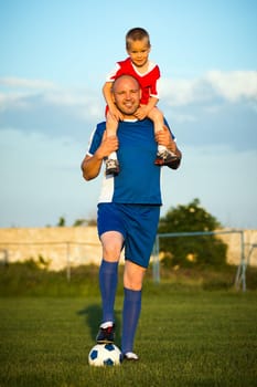 The happy family father and son is playing soccer outdoors on the green grass playground on soccer playing field.