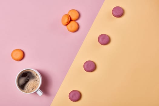 Still life with cup of coffee and delicious macaroons lying on background consisting of two colores pink and yellow. Top view with copy space. Design element for menu of cafe