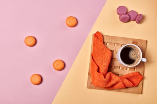 Still life with cup of coffee and delicious macaroons lying on background consisting of two colores pink and yellow. Top view with copy space. Design element for menu of cafe