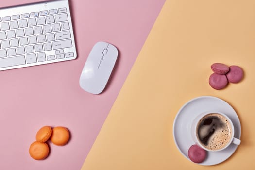 Cup of coffee, macaroons, computer keyboard and mouse on background consisting of two colores pink and yellow. Top view with copy space. Design element for menu of cafe, internet cafe, web, workplace.
