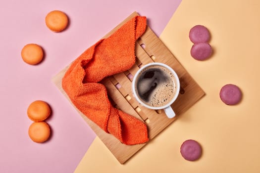 Still life with cup of coffee and delicious macaroons lying on background consisting of two colores pink and yellow. Top view. Design element for menu of cafe