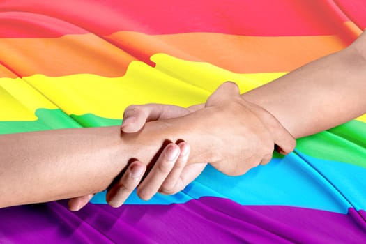 Two gay couple hands holding each other by the wrists with rainbow flag background. LGBT concept