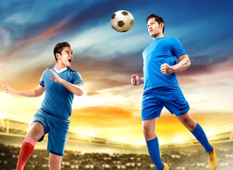 Two asian football player man jump in the air and duel heading the ball on football field at stadium