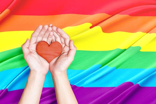 Human hands holding heart with rainbow flag background. LGBT concept