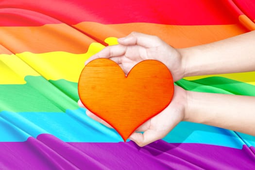 Human hands holding heart with rainbow flag background. LGBT concept