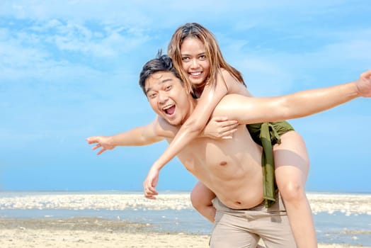 Happy asian man carrying a girl on his back in the beach. Summer vacation