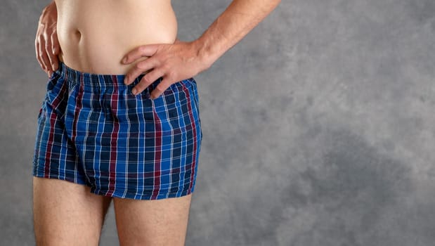 man in blue plaid boxer shorts in front of gray background