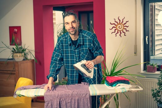 man with iron on ironing board with clothers in living room