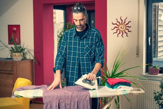 man with iron on ironing board with clothers in living room