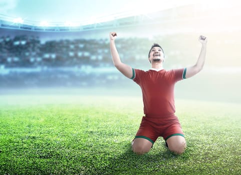 Football player man celebrate his goal with raised arms and kneeling on the football field at stadium