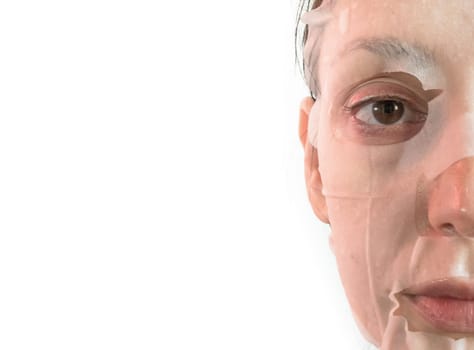 Young woman is applying a cosmetic tissue mask on his face on a white background. Beauty treatment and lifestyle concepts. Space for text.