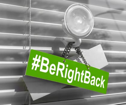 Hashtag "Be right back"" on a glass door with a white, closed venetian blind. It can be used for business concepts or backgrounds."