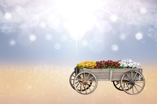 Happy spring or greeting card composition. Closeup of decorative old big wooden cart or waggon with many colorful flowers over abstract light sunny day background. Space for your design.