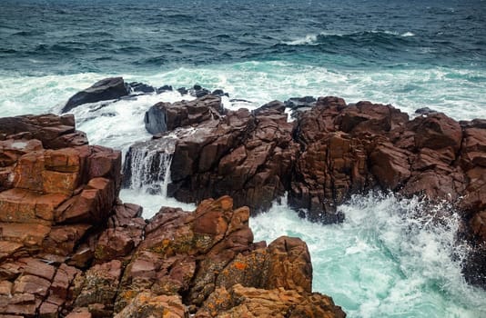 Stormy sea waves crash against a rocky shore. Waves crashing over rocks. Scenic seascape.
