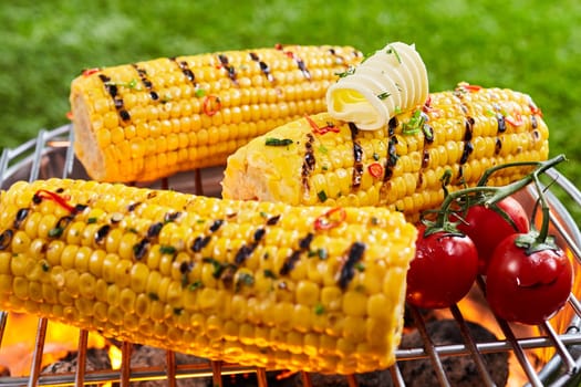 Delicious grilled corn on the grille with cherry tomatoes and a curl of butter, being prepared outdoors