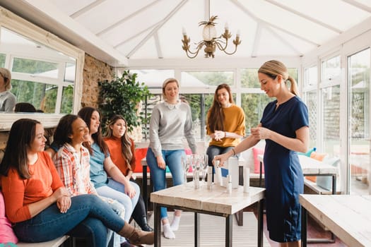 Small group of women with a mixed age range sitting together at a beauty product party. The beauty product sales representative is standing talking about the products.