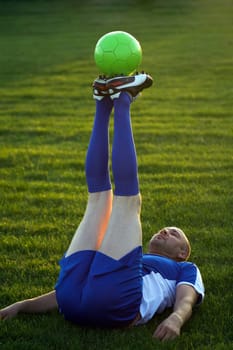 The senior soccer player is practicing soccer practices with soccer ball lying down on lawn outdoors.