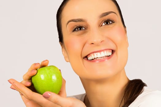 Beautiful smiling woman with white healthy teeth is holding a green apple on white background, studio shot, health care and dental care concept.