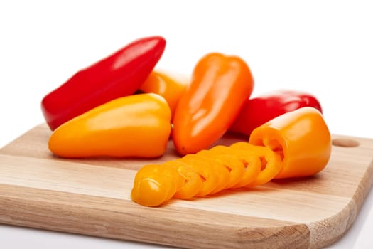 Fresh ripe peppers lying on wooden cutting board on a white background.
