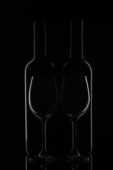 Silhouette of two wine bottles and two empty wineglasses on a black background with reflection. Contour with gradient and highlights