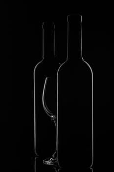 Silhouette of two wine bottles and empty wineglass on a black background with reflection. Contour with gradient and highlights