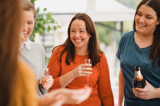 Small group of female friends celebrating at a house party. They are enjoying a glass of champagne, laughing and smiling.